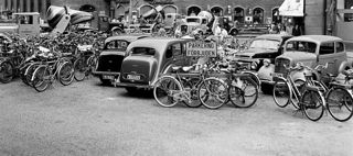 Cyklar uppställda bland bilar framför Konserthuset. 