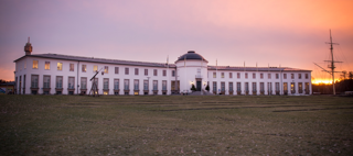 Bilden föreställer ett vitt, längt, böjt hus i morgonljus.