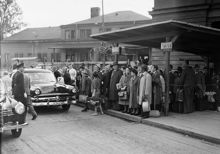 Södra delen av Centralplan. Folksamling köar till taxibilar. Provisorisk brädklädd körbana och trottoar täcker centralplan, pga. att arbete för t-banan pågick därunder