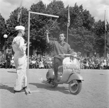Vespa-tävling i Kungsträdgården. I tävlingen gällde det att bland annat flytta ett glas vatten. En fransman rev allt som gick att riva och folket jublade då han lyckades få allt vattnet i glaset i ansiktet