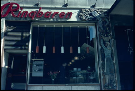 Genom caféterians fönster syns hängande lampor och en kund.
