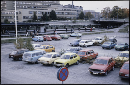 Vy mot parkering med många färgglada bilar och Liljeholmens tunnelbanestation år 1978