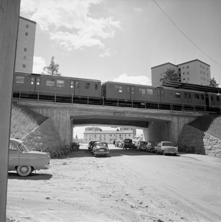 Bilar som står parkerade under en bro där tunnelbanan far förbi.