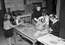 Engelska skolan. Lärare och elever rör ihop en smet i en gryta i klassrummet, troligen papier mache eller liknande