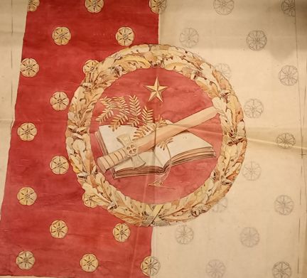 En skiss med halvt röd, halvt vit botten. I skissen finns massor av små gula blommor. I mitten av skissen finns en eklövskrans. I mitten av kransen ligger en uppslagen bok. Ovanpå boken finns ett svärd och en ormbunke. Ovanför boken finns en stjärna.