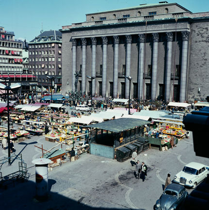 Färgfoto av Konserthuset vid Hötorget med marknadsstånd i förgrunden.