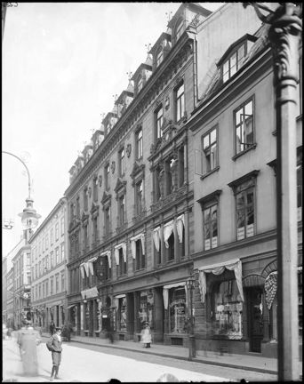 Fasader med skyltfönster i gatuplan. Människor passerar.