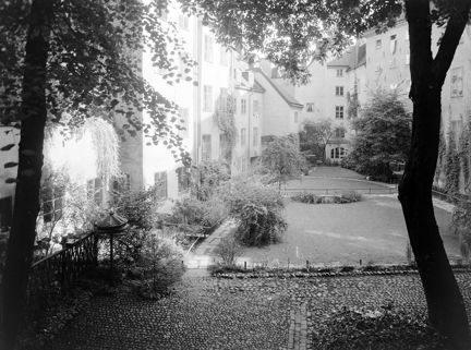 Innergård med gräsmattor, träd, buskar och kullersten.