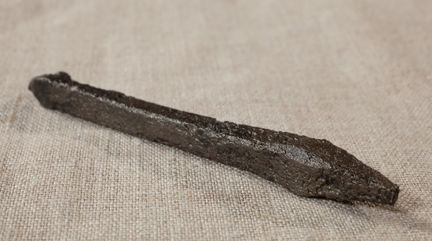 Armborstpil av dalpilstyp i järn. Fotograferat på nära håll mot en grålila bakgrund.