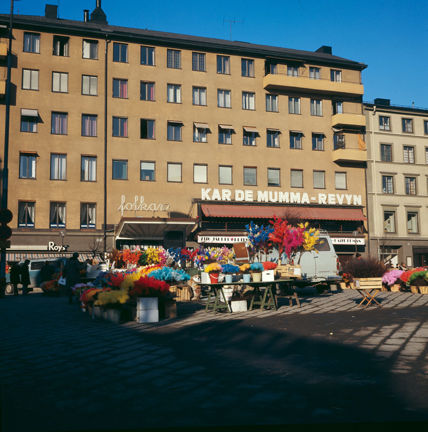 På ett torg säljs det färgglatt påsk- eller fastlagsris. I bakgrunden syns en större stenbyggnad med slätputsad fasad. På ett utskjutande baldakintak står det "Folkan" vilket är namnet på teatern i byggnaden. På fasaden står det "Kar de mumma revyn" med stora bokstäver. 