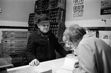 Norra Smedjegatan 5. Man som handlar i Maja Erikssons mjölkbutik. Maja Eriksson skriver in summan i sin kassabok.