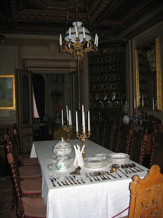 Bord, vit duk, höga ekstolar, takkrona, mörka väggar