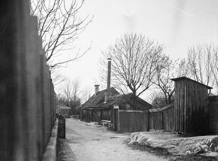 Åsögatan 159 västerut. Nuv. Åsögatan 213. På båda sidor om gatan syns träplank och låg träbebyggelse. 