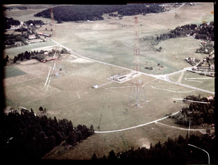Flygbild över gräs, skog och två radiomaster