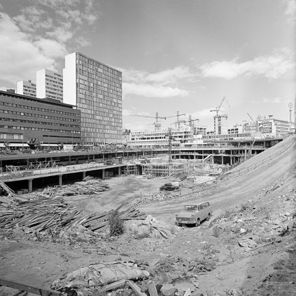 I förgrunden en stor byggrop med fordon i, i bakgruden moderna höghus och byggkranar