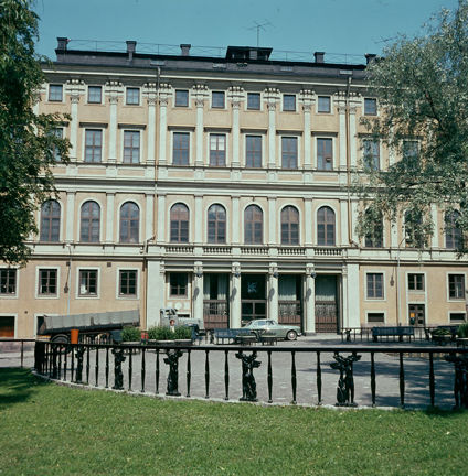 Framför teatern syns gräsmatta och ett staket vid Mosebacke torg. Utanför teatern står en bild och en lastbil parkerade.