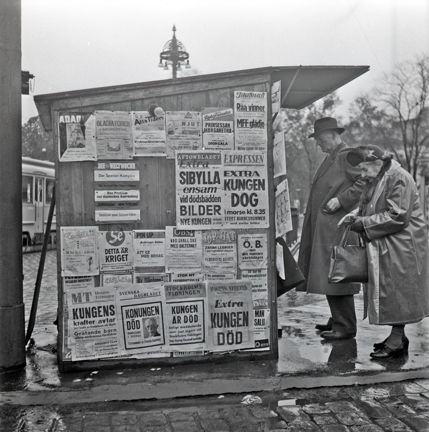 Foto taget från sidan på kiosk. Två äldre personer i färd med att handla.