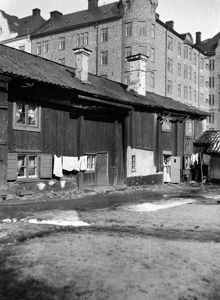 En kvinna med ett barn står i dörröppningen mot gården vid Fatbursgatan 1. Nu Fatbursgatan 29 A, kv. Färdknäppen. Bostadshuset i bakgrunden ligger vid hörnet av Fatbursgatan och Timmermansgatan 43